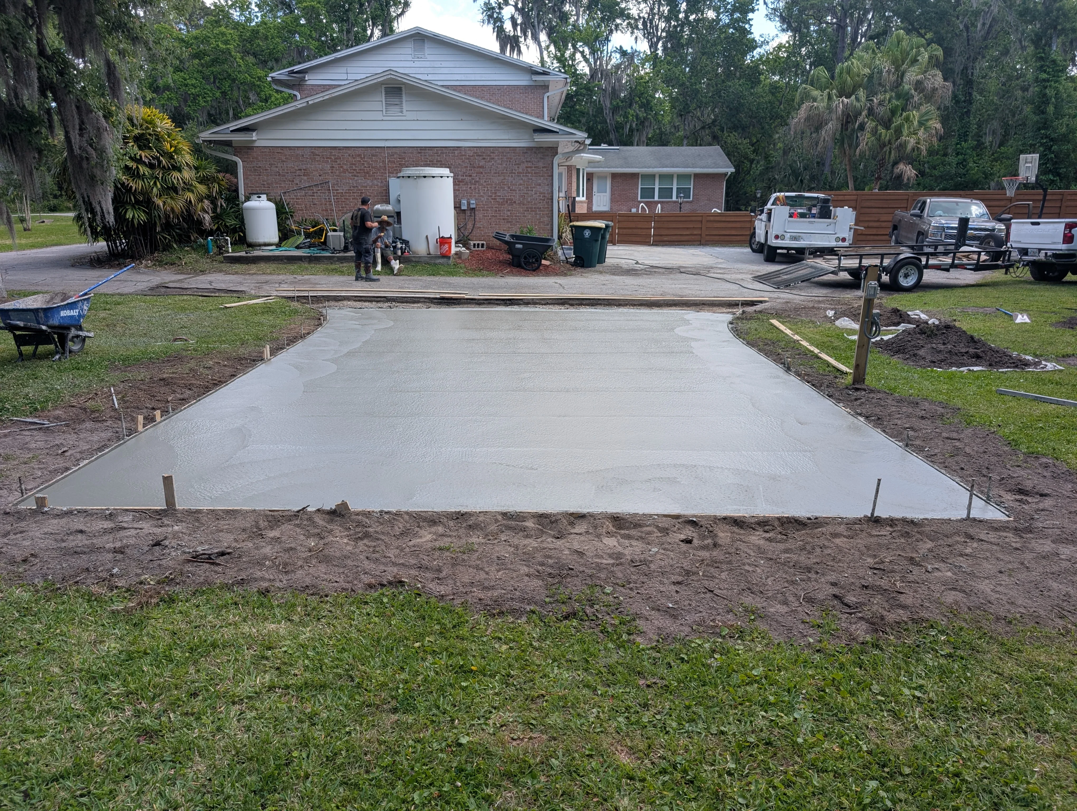 Freshly poured concrete driveway with edge forms and control joints in front of brick home