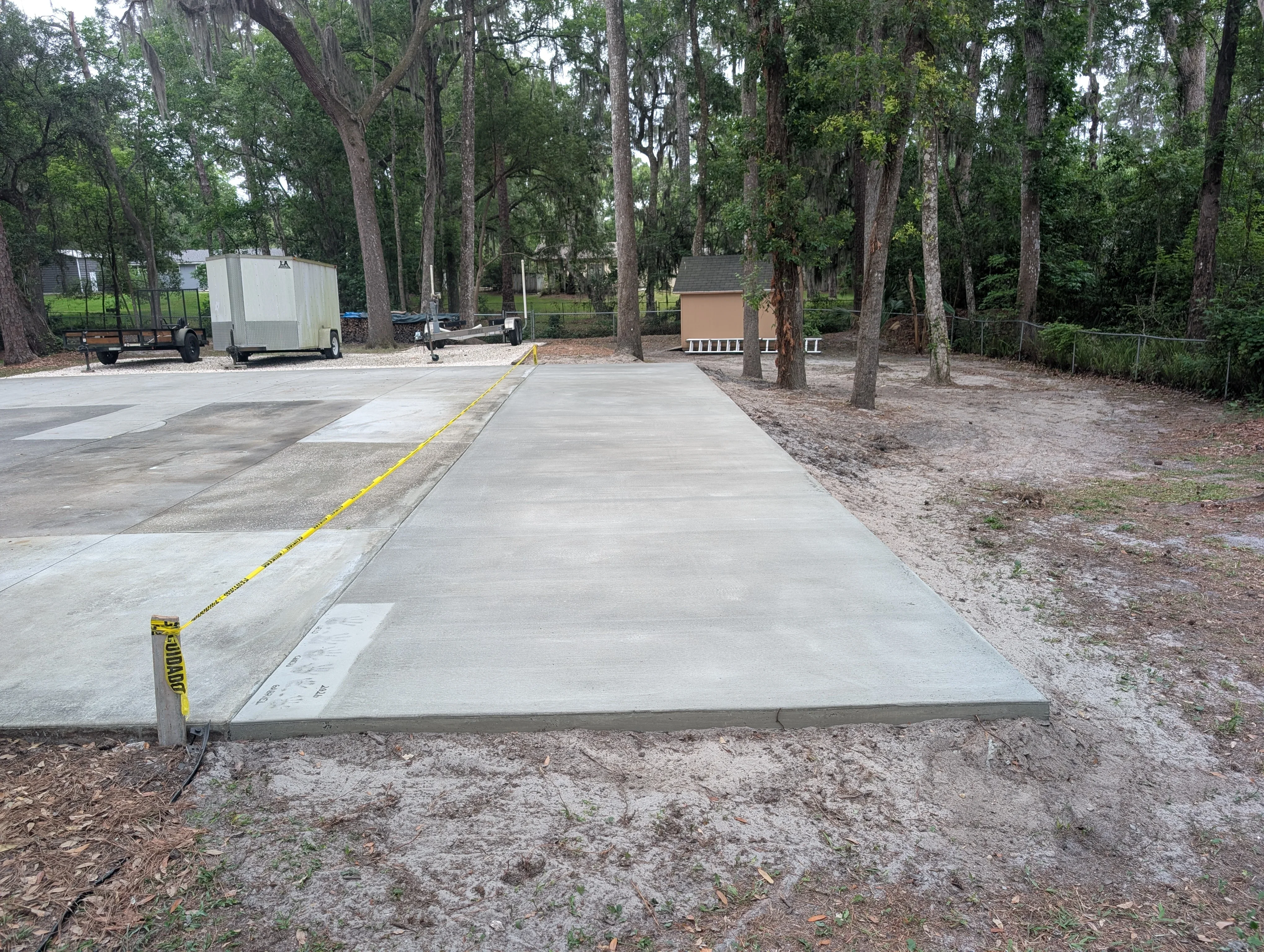 Newly poured concrete pad with finished surface and yellow caution tape marking edges