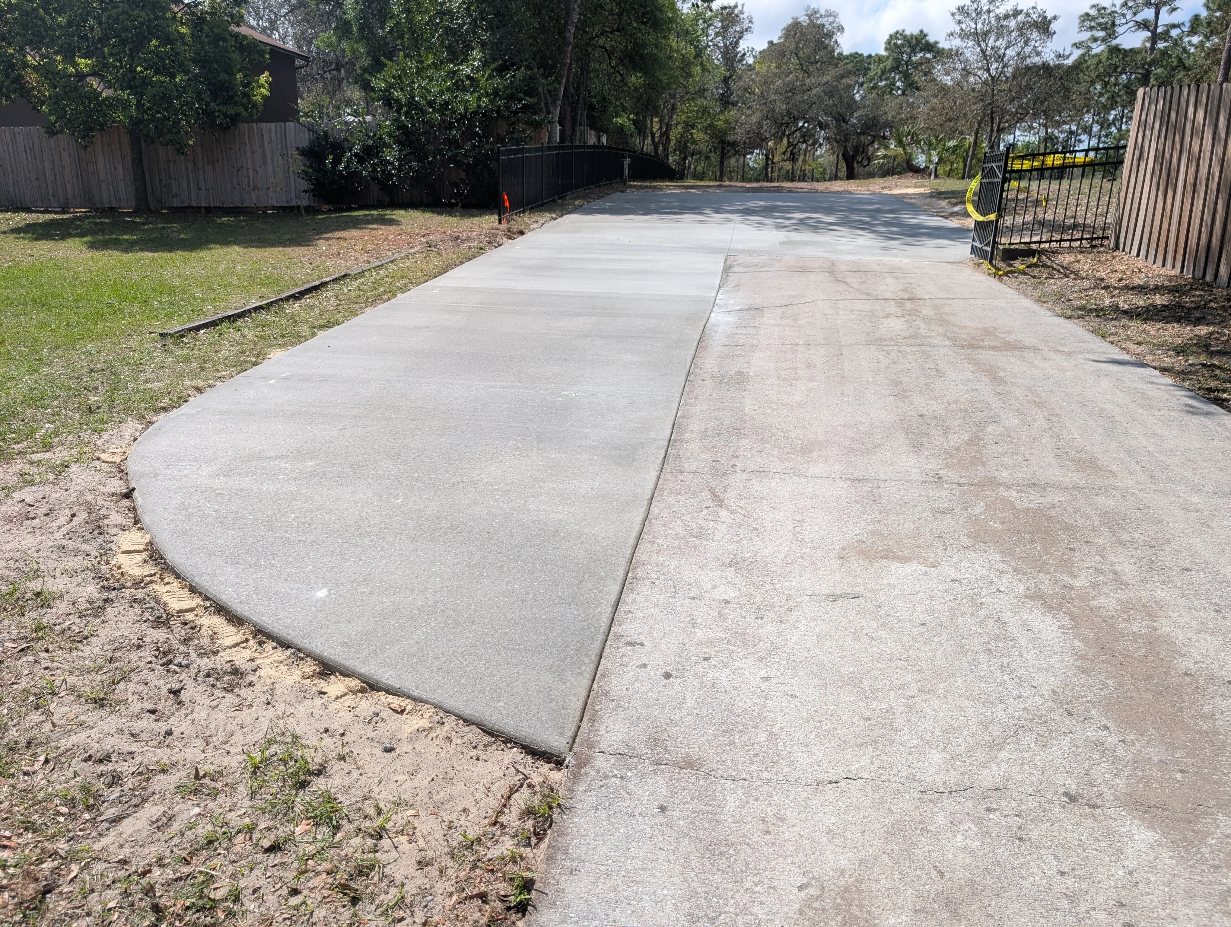 New concrete driveway with control joints, curved entry, adjacent to metal fencing and landscaping