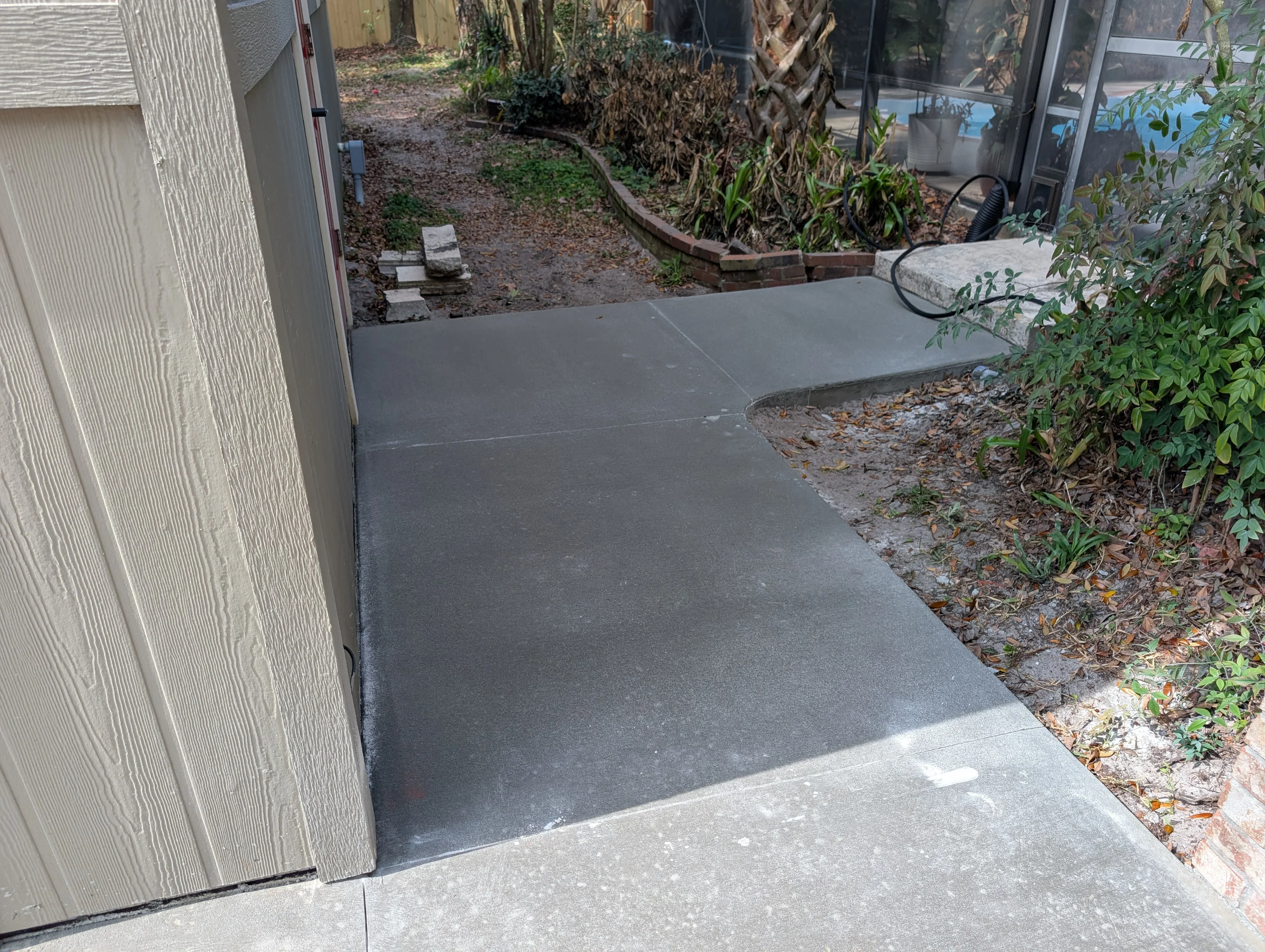 Gray concrete patio with clean edges next to house and landscaping