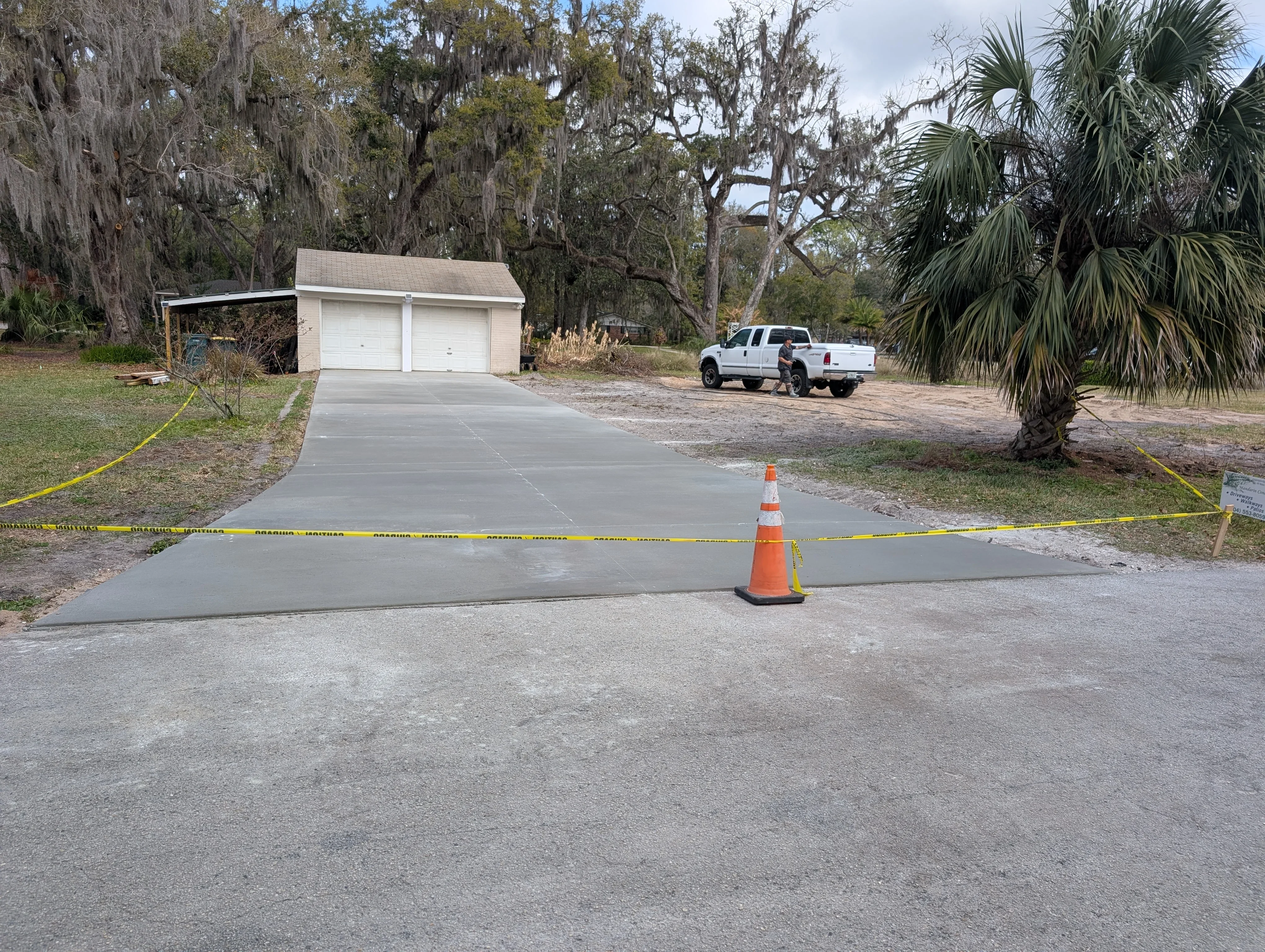 Fresh concrete driveway extension with two-car garage and mature oak trees
