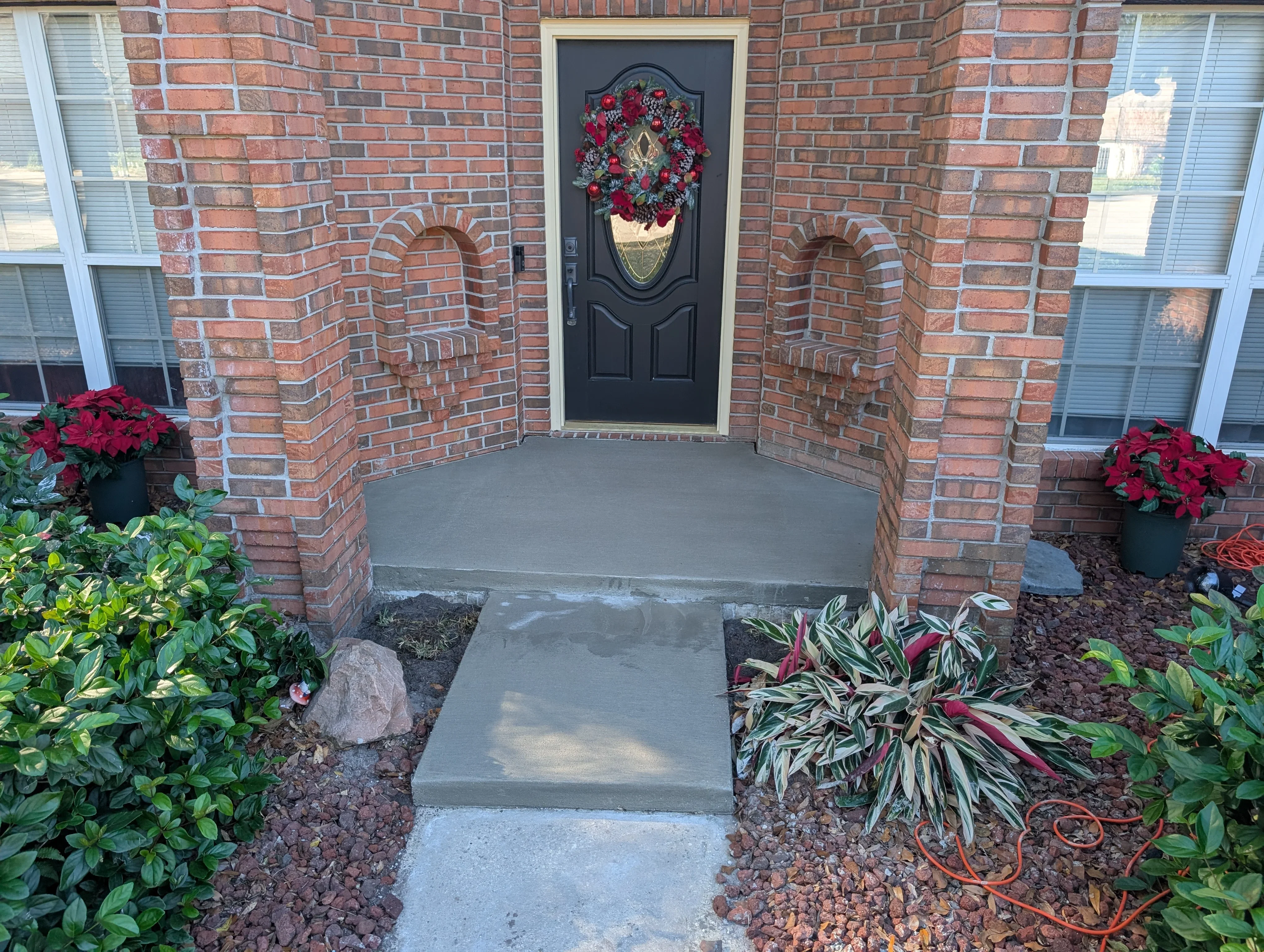 Gray concrete entryway pad and walkway with brick archway and landscaping