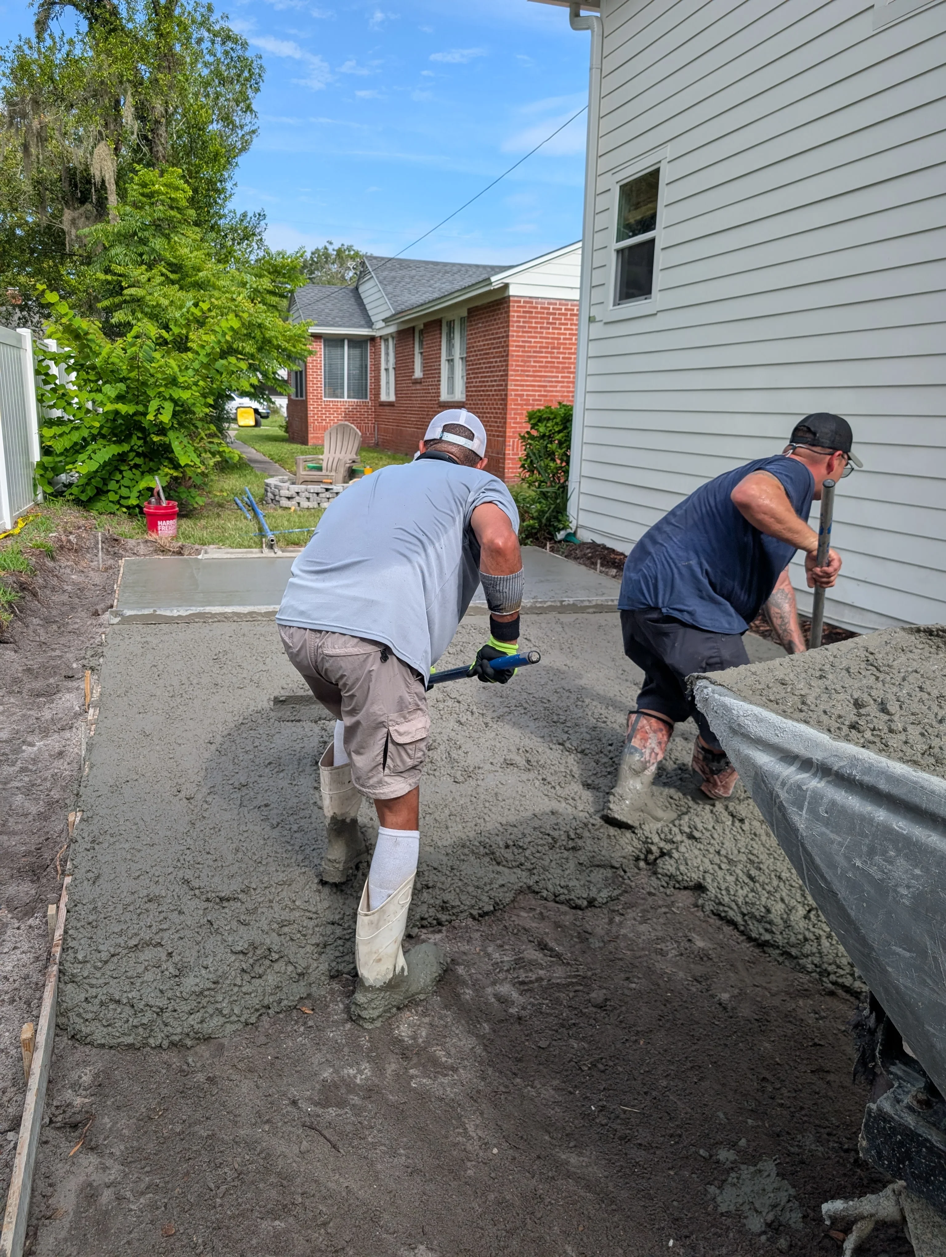 Two workers finishing concrete driveway with tools, concrete forms visible along edges