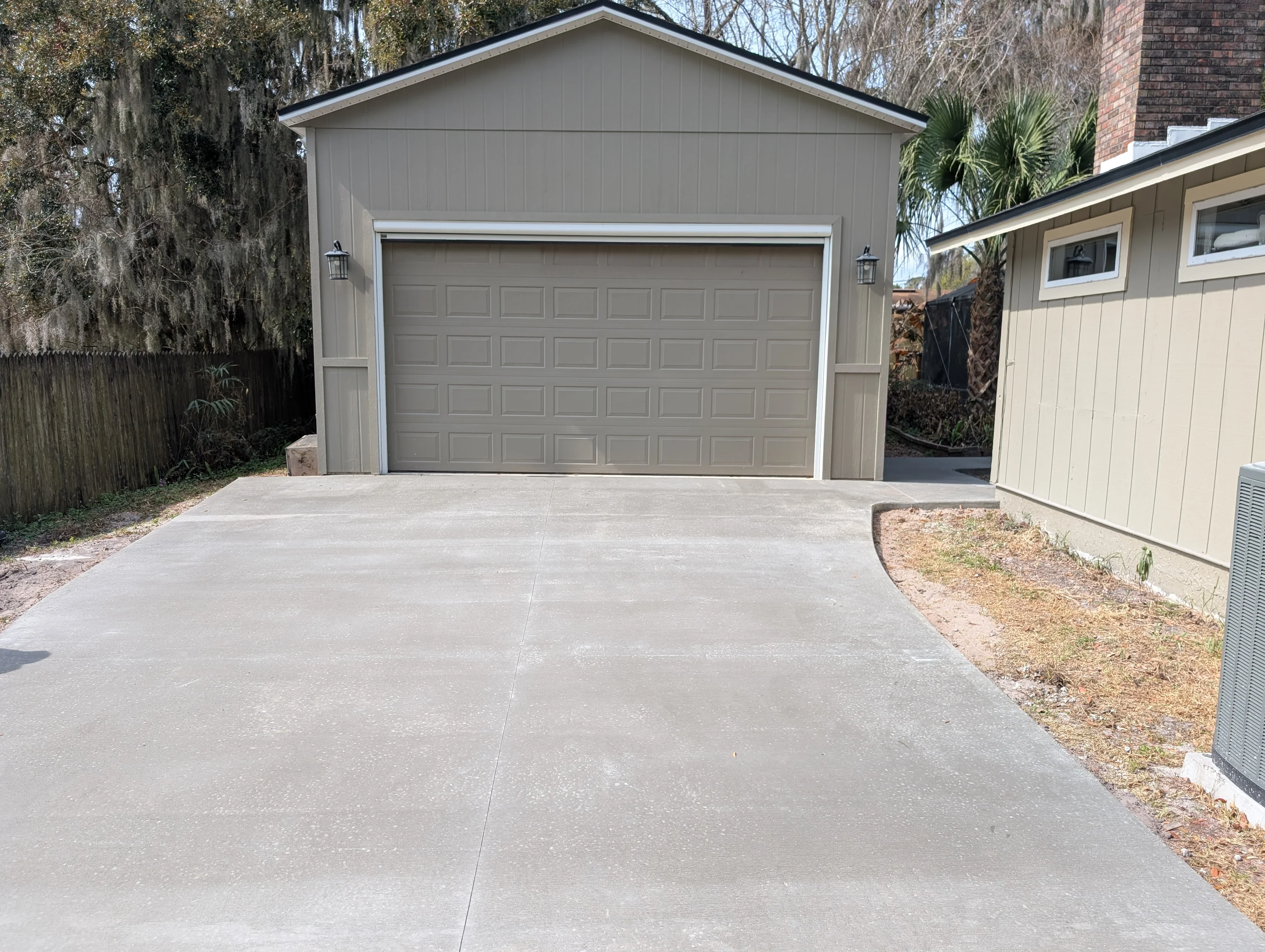 Finished concrete driveway with control joints in front of gray garage structure